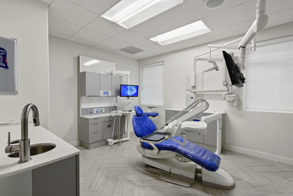 Treatment room with a blue chair, sink and overhead monitors