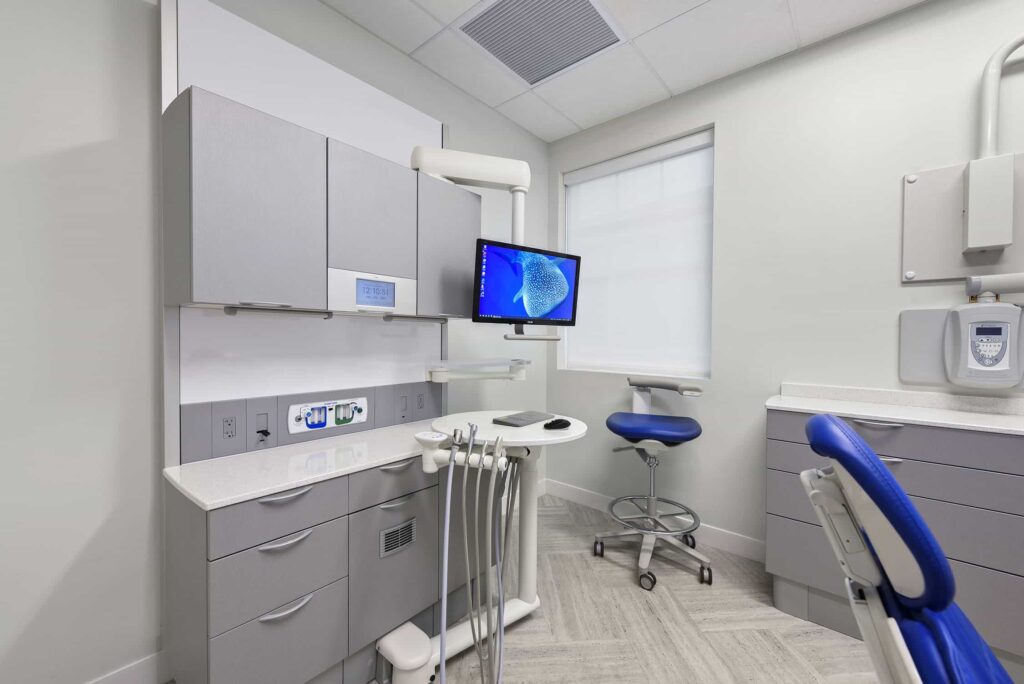 Treatment room with gray cabinets, a wall monitor and a blue dental chair