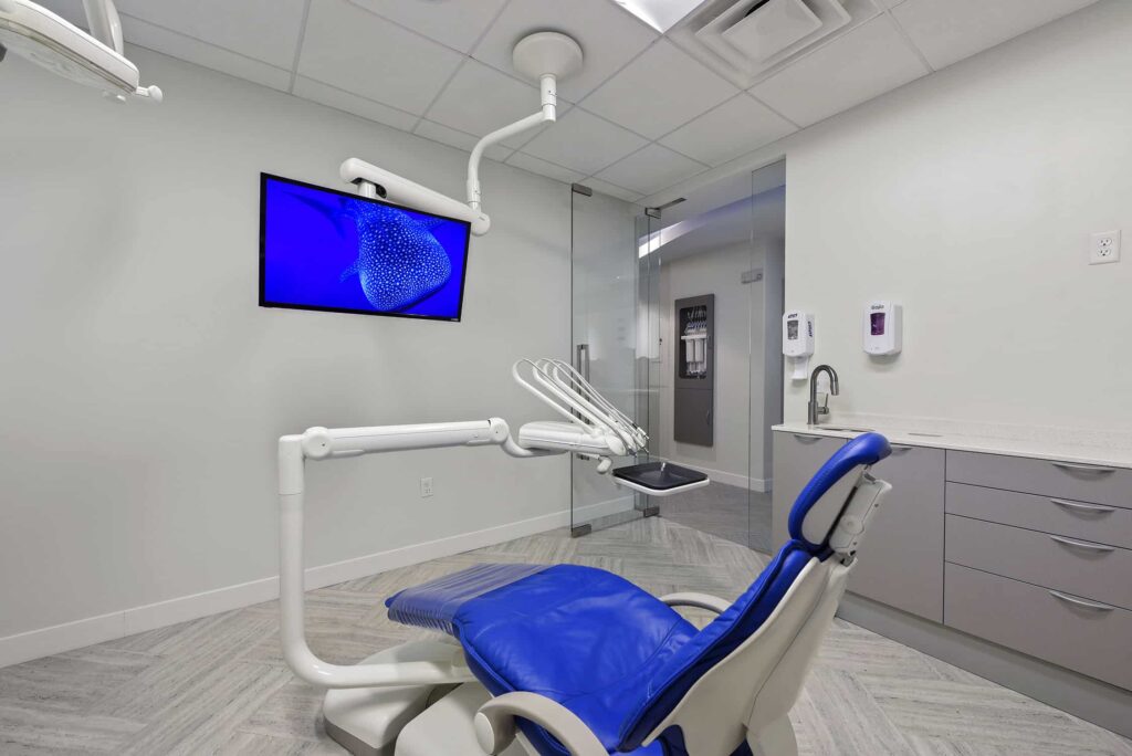 Blue dental chair beneath a wall monitor showing a jellyfish