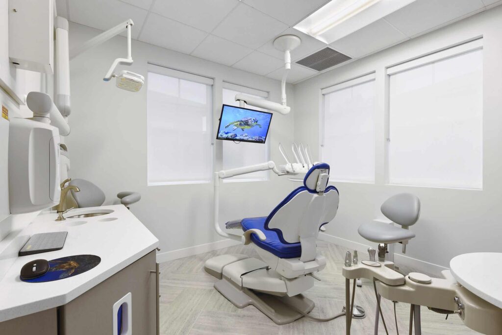 Bright treatment room with a blue dental chair facing the windows