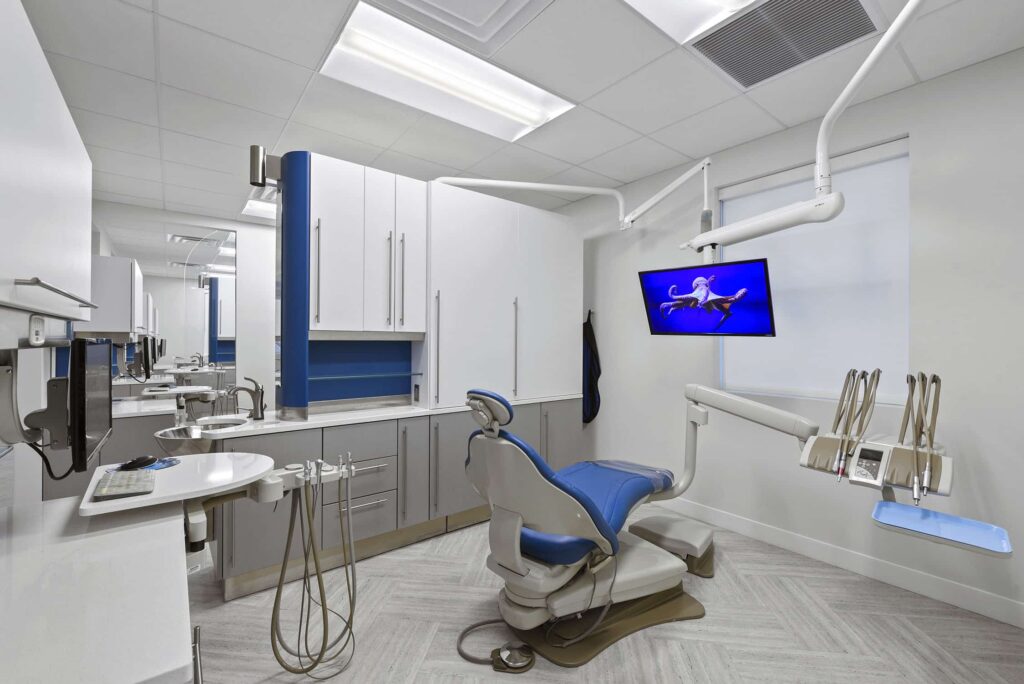 Treatment room with a blue chair, monitor and dental instruments
