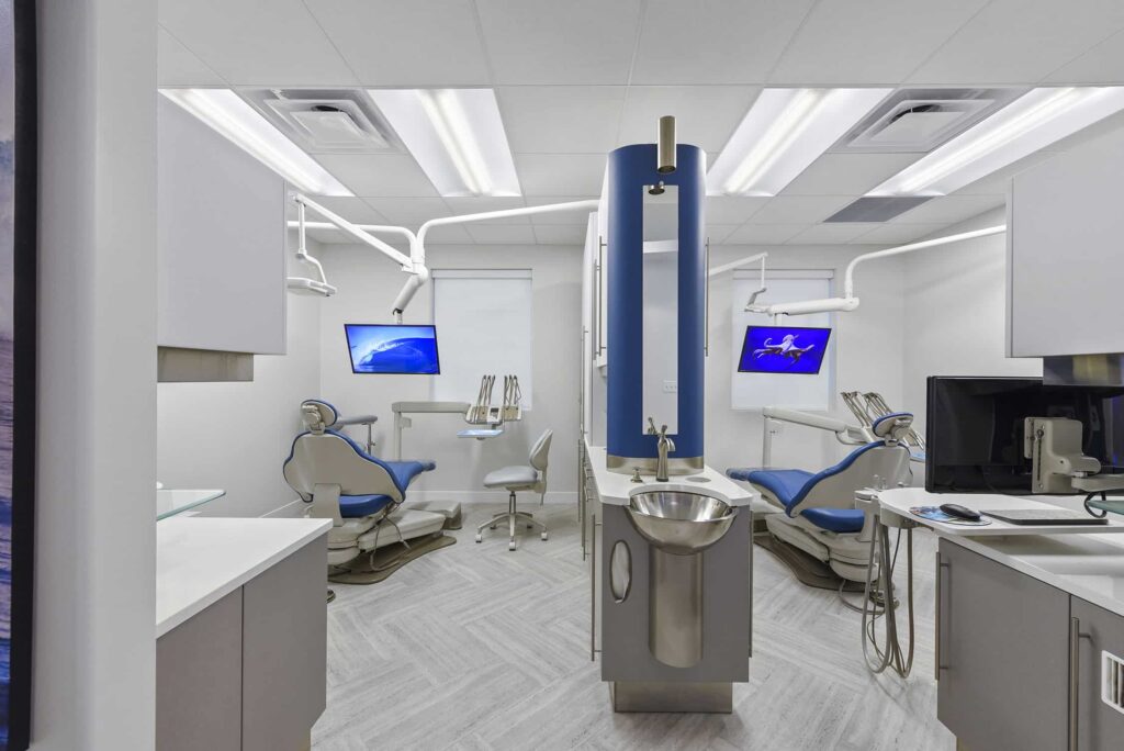 Open treatment area with two blue dental chairs and a central sink station