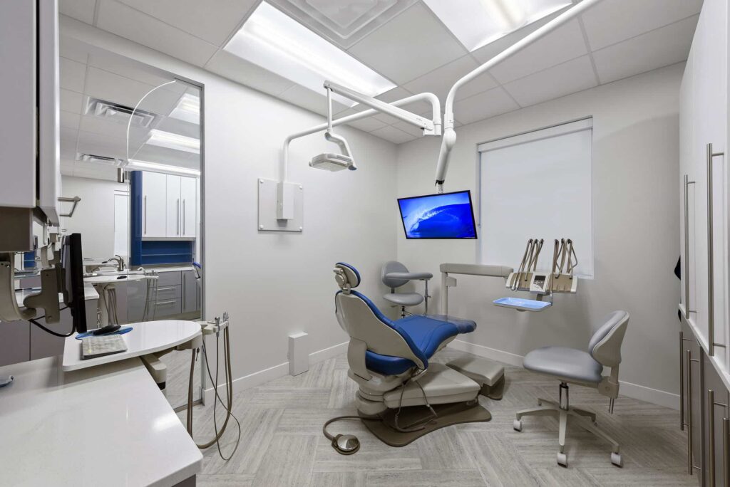 Treatment room with a blue dental chair, overhead light and wall monitor
