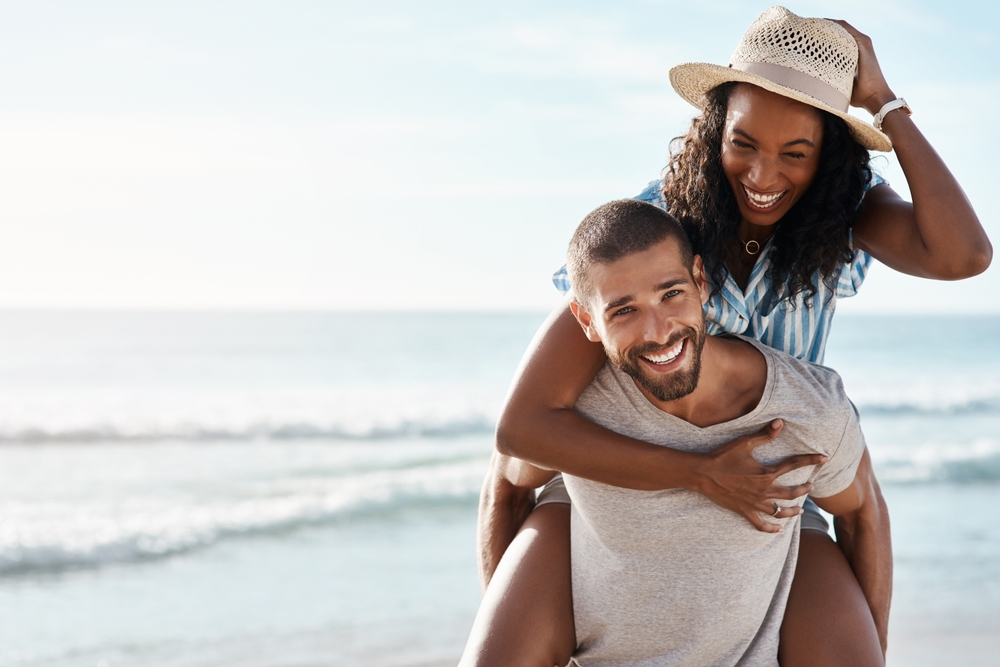 Smiling couple on the beach, the woman riding piggyback on the man