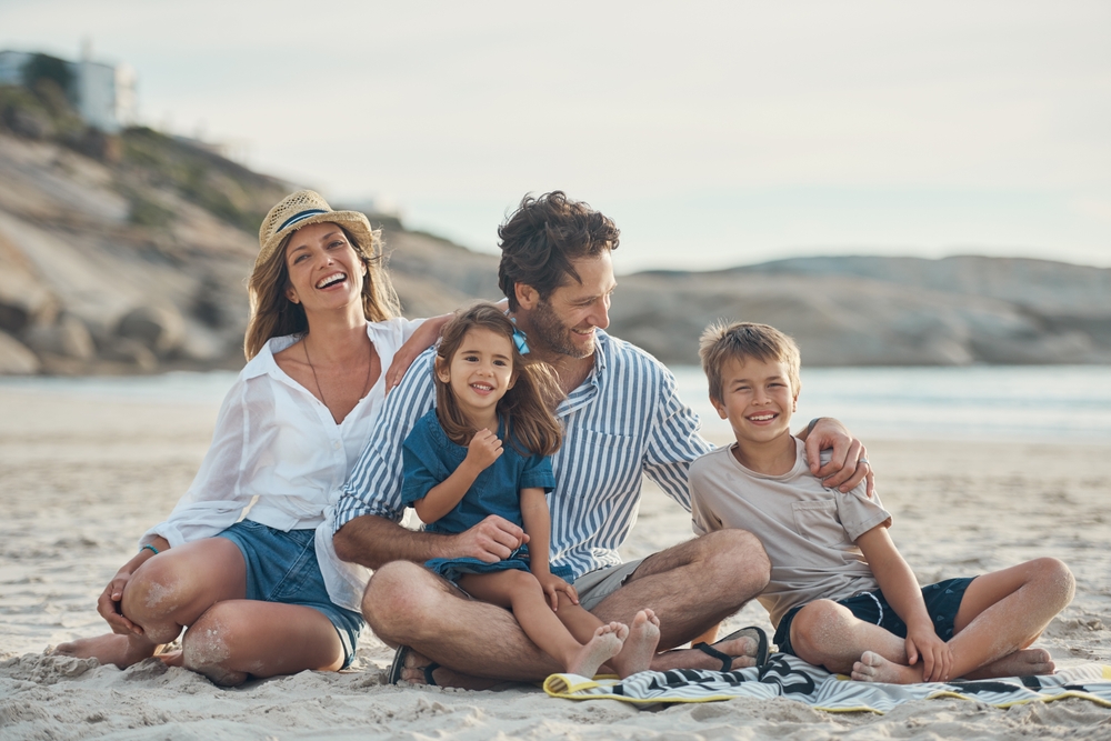 Family of four sitting together on a blanket on the beach