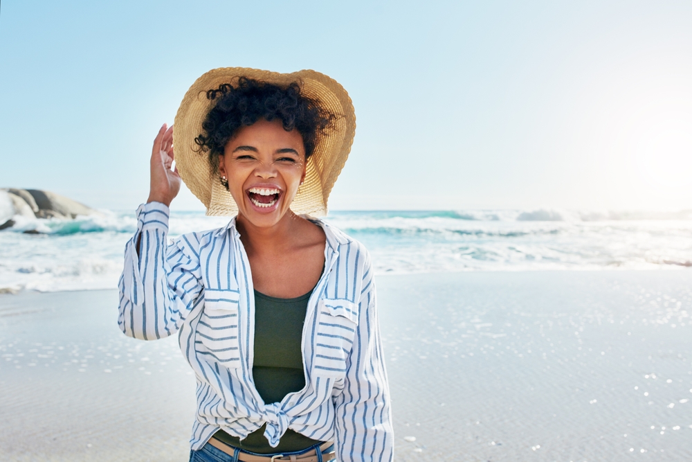 Laughing woman in a straw hat and striped shirt on the beach