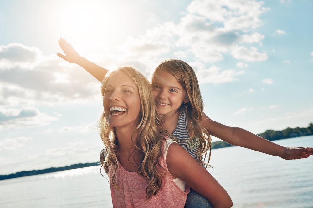 Relaxed, smiling woman giving a girl a piggyback ride by the water