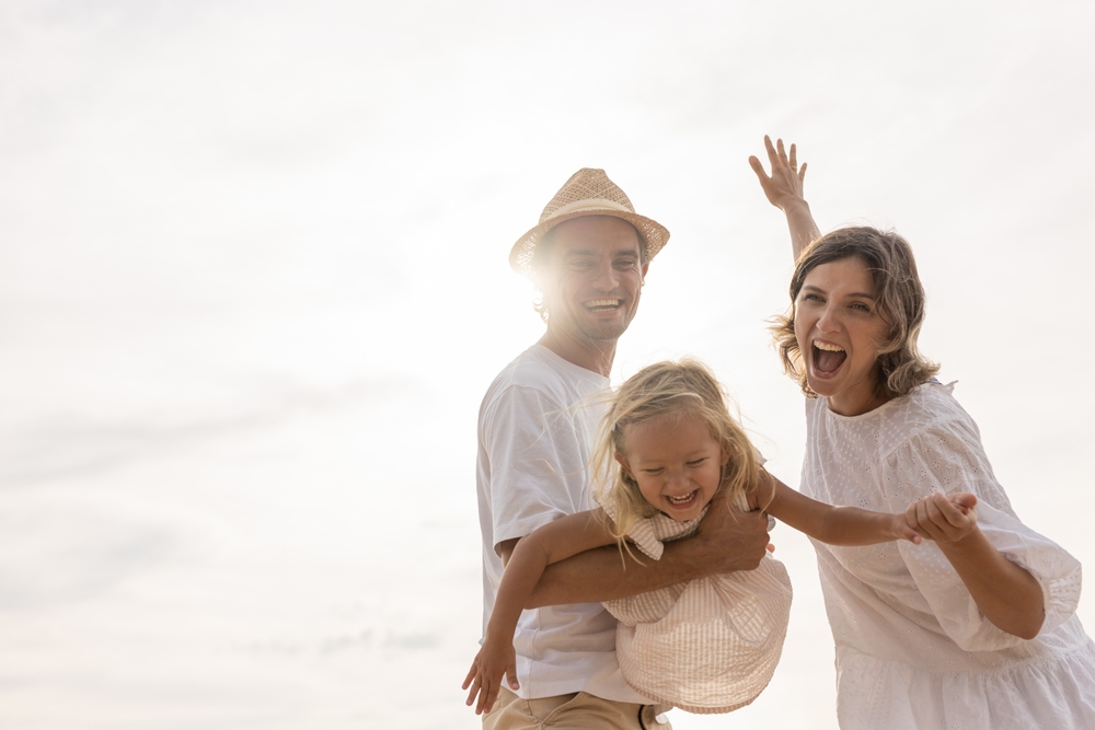 Happy family playing on the beach, the father swinging his daughter