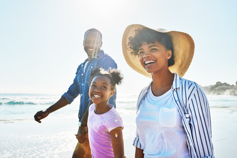 Smiling family of three walking on the beach, the mother in a straw hat