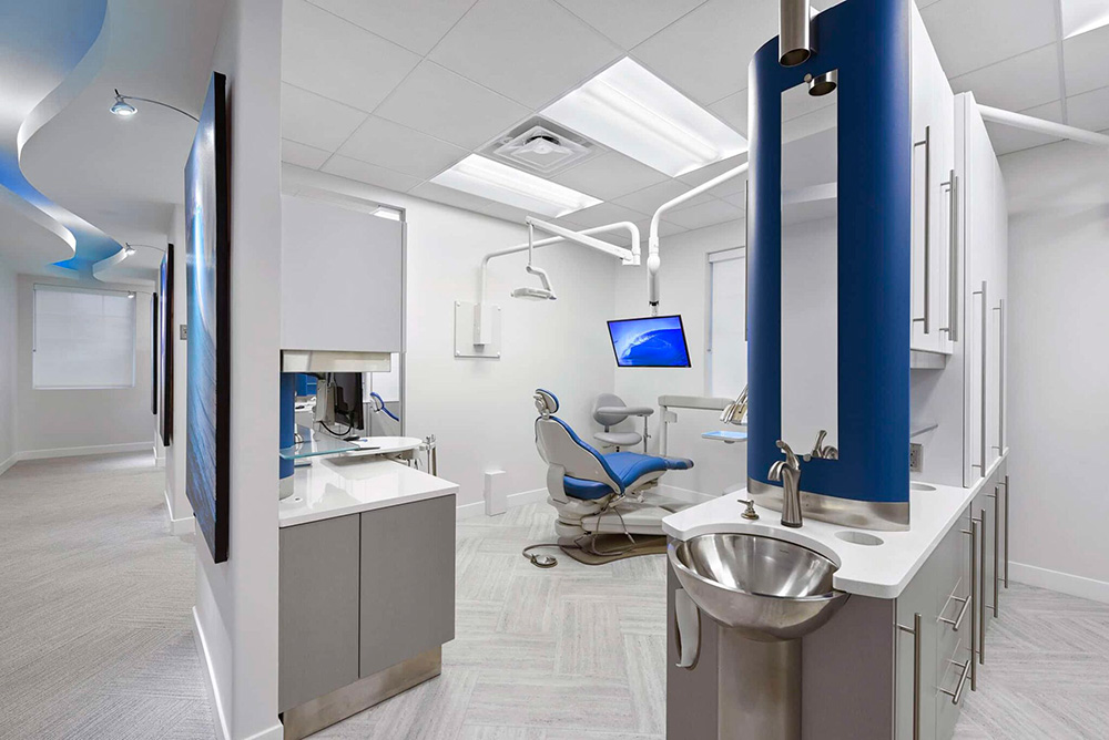 Treatment bay with a blue dental chair and stainless steel sink column